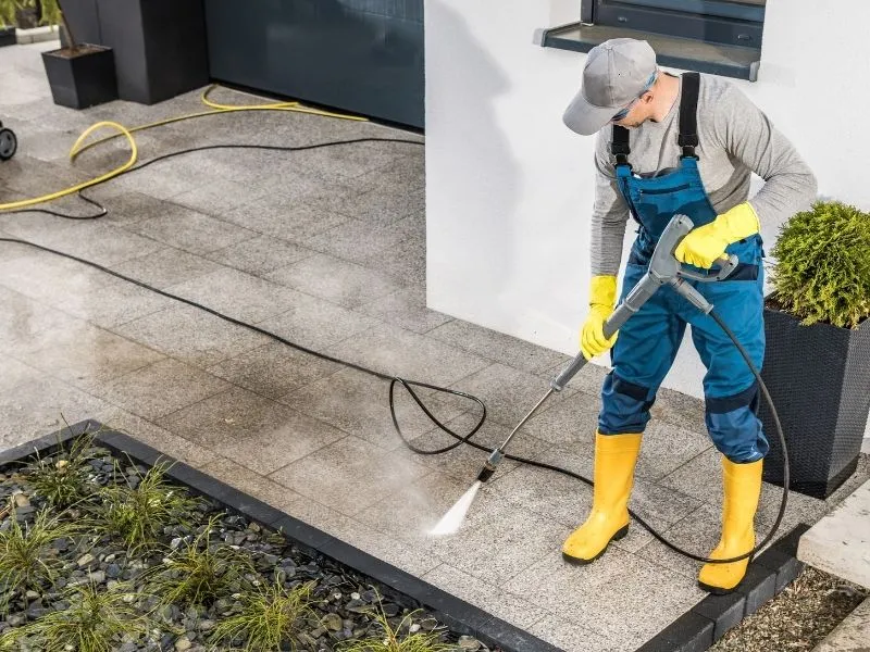 Worker in overalls and rubber boots pressure washing paving stones