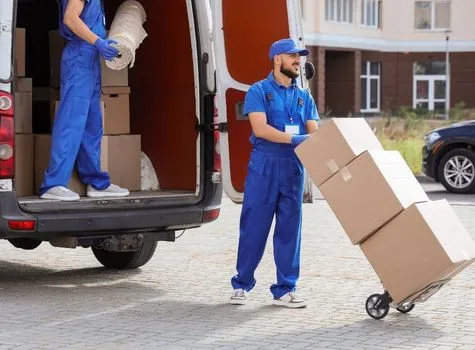 Movers in blue uniforms unloading a van and wheeling boxes on a hand truck