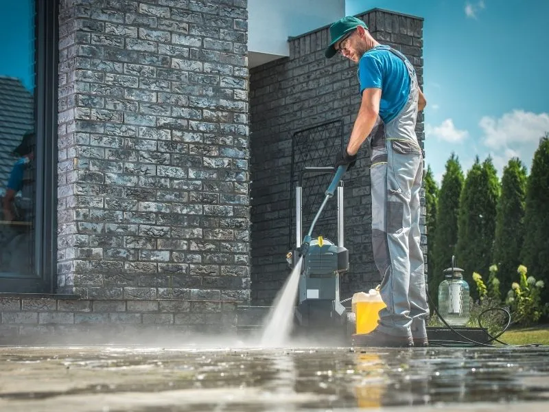Worker pressure washing a patio in front of a dark brick wall