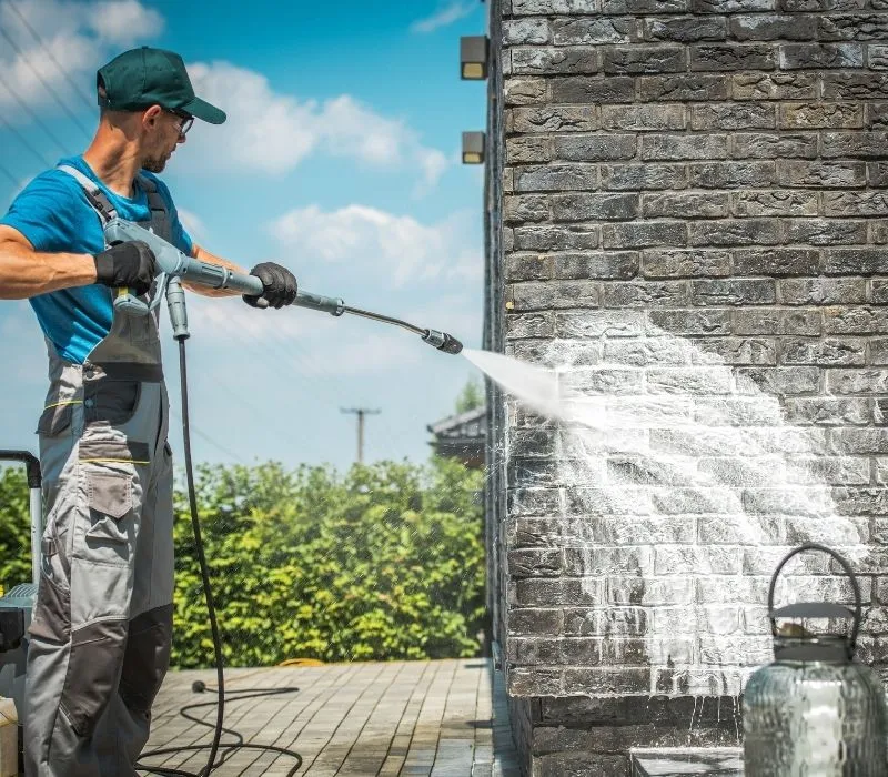 Worker pressure washing a brick wall