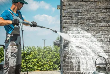 Worker pressure washing a brick wall