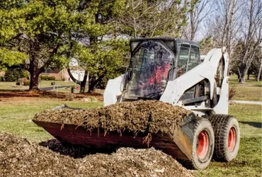 Bobcat skid steer loader carrying a bucket of soil across a yard