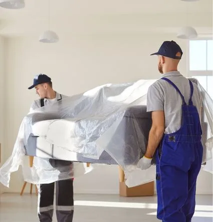 Two movers carrying a plastic-wrapped sofa through an empty room