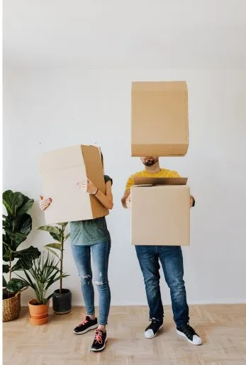 Two people carrying tall stacks of cardboard moving boxes