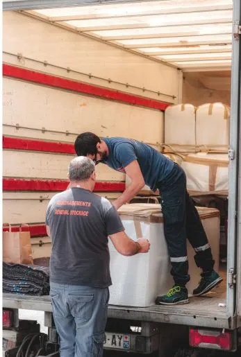 Two workers loading a large white item into the back of a box truck