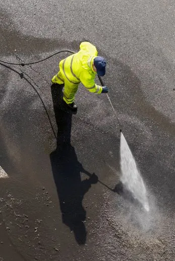 Worker in protective rain gear pressure washing a dark surface